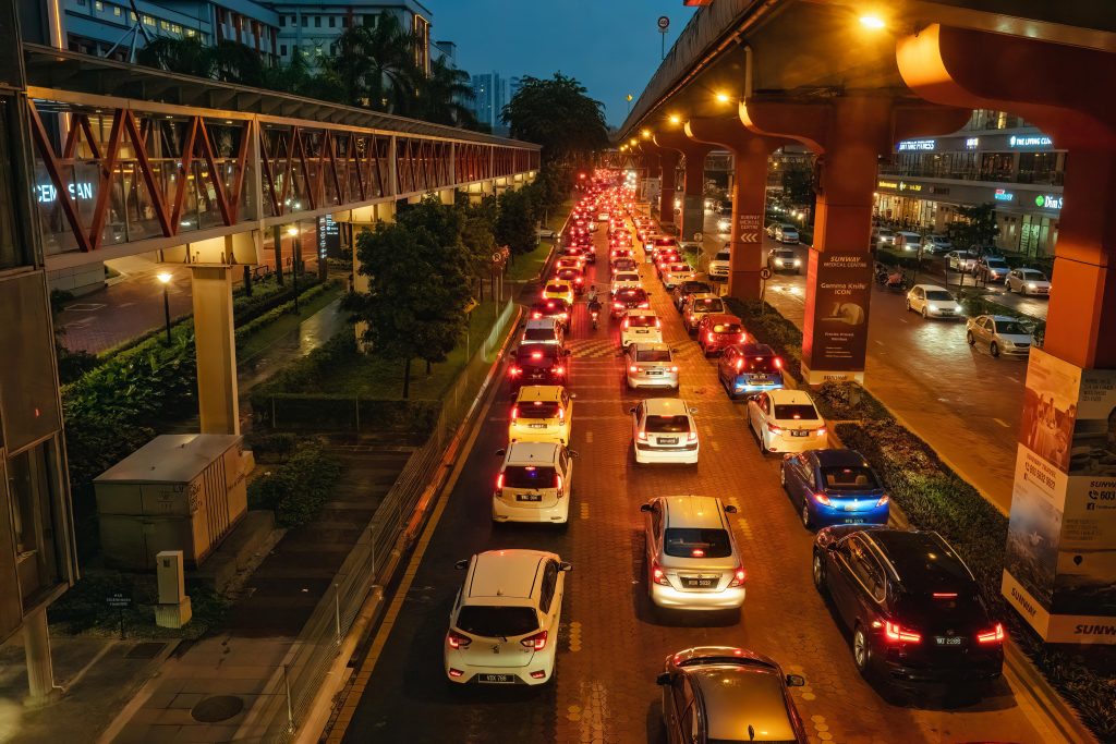 Evening traffic jam in Kuala Lumpur with cars on a busy urban road under lit bridges.
