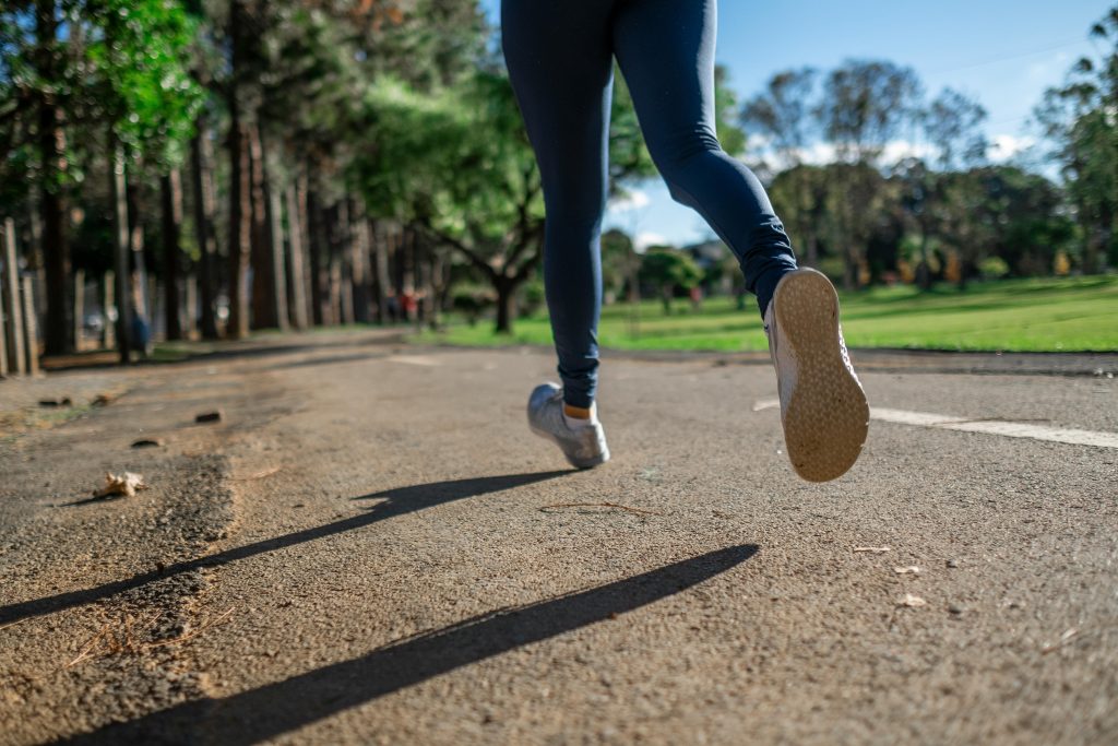 親愛的,如果控制的極致是學會放手? A woman running outdoors on a sunny day along a scenic park trail, focusing on fitness and health.
