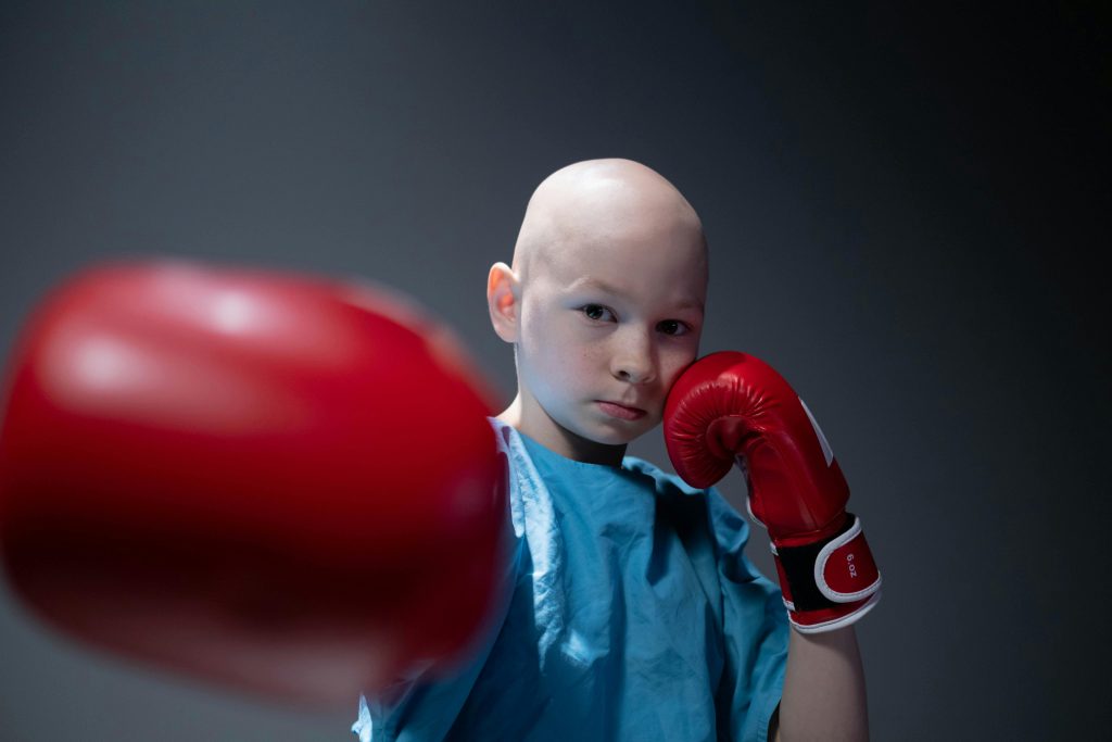 在中山南路上,跑過孩子們的明天 Bald child in boxing stance wearing hospital gown and red gloves, symbolizing strength.