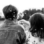 把二十年揉進垃圾桶的那一天,我才終於聞到自由的氣味 Back view of kids playing with dandelion seeds in a field, captured in monochrome.